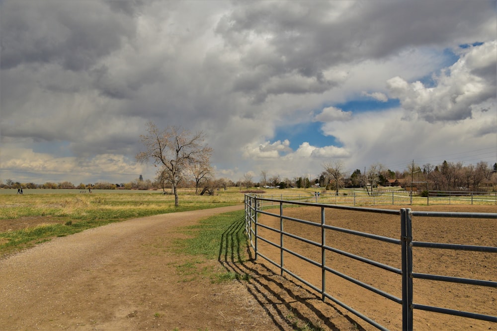 a dirt road with a fence and a field in the background