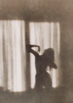 A silhouette of a woman by a window, bathed in natural light, evoking mystery.