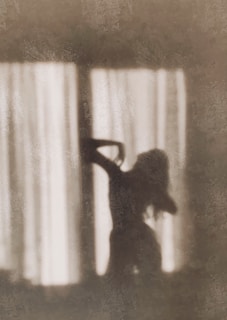 A silhouette of a model posing gracefully by a window with soft natural light streaming in.