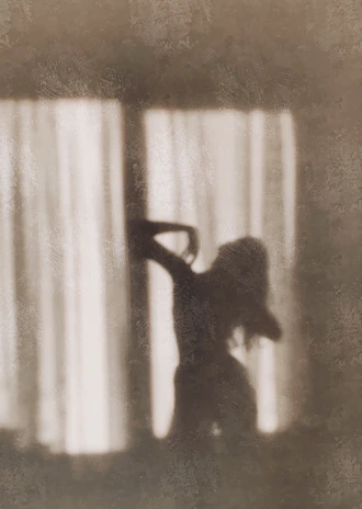 A silhouette of a woman by a window, soft light highlighting her curves.
