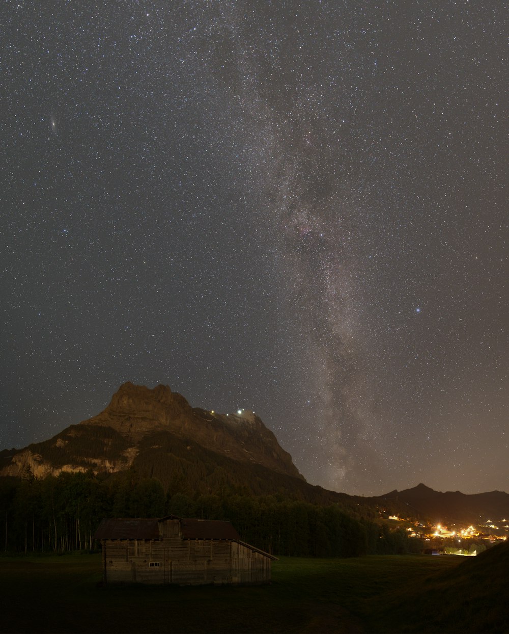 the night sky over a mountain with a house in the foreground