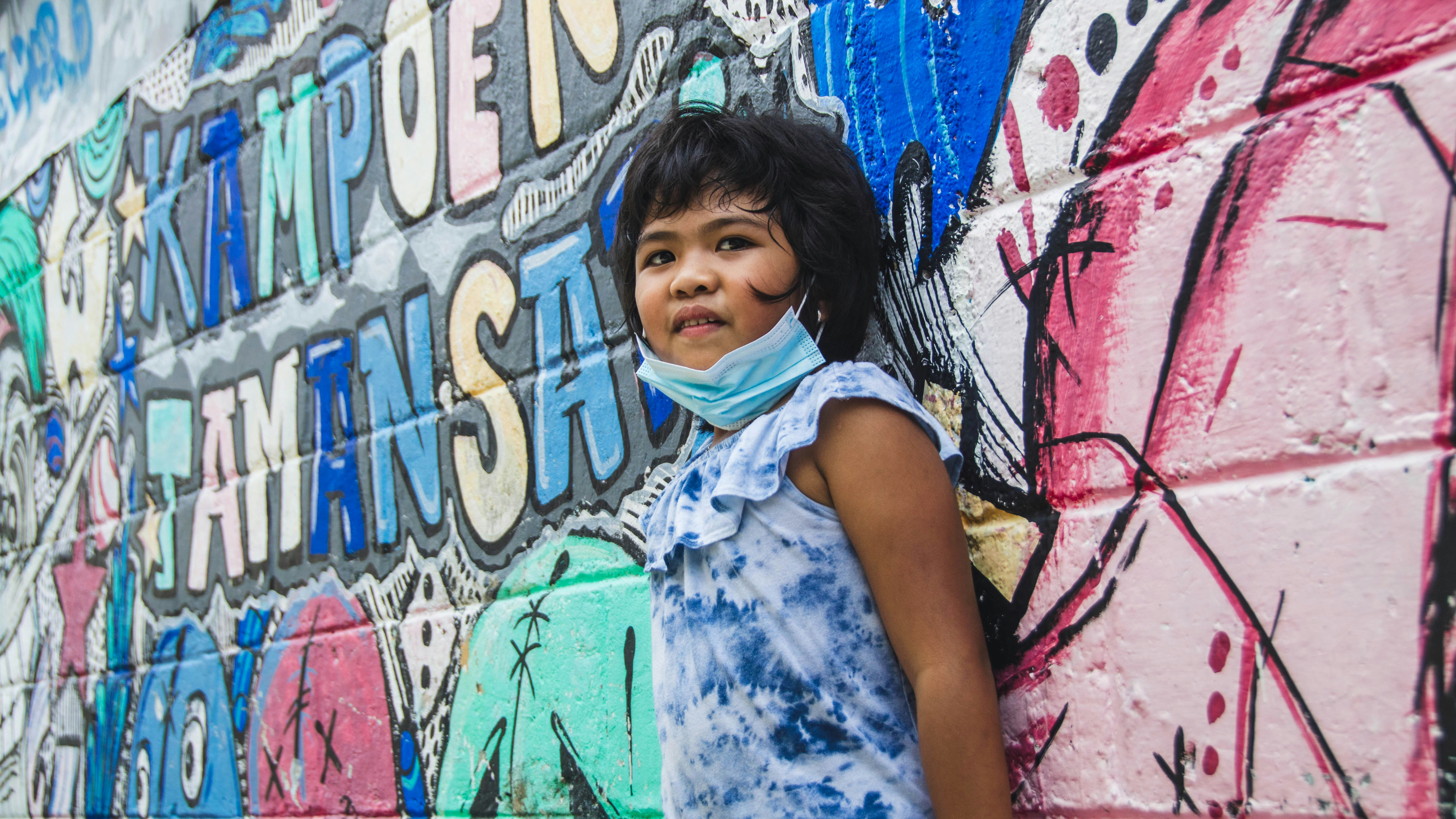 a little girl standing in front of a wall covered in graffiti