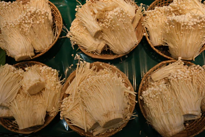 Bundles of delicate enoki mushrooms with long stems and tiny caps arranged on a rustic wooden surface.