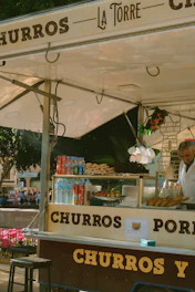 A vibrant fast-food style churro stand with red and yellow branding and customers enjoying fresh churros.
