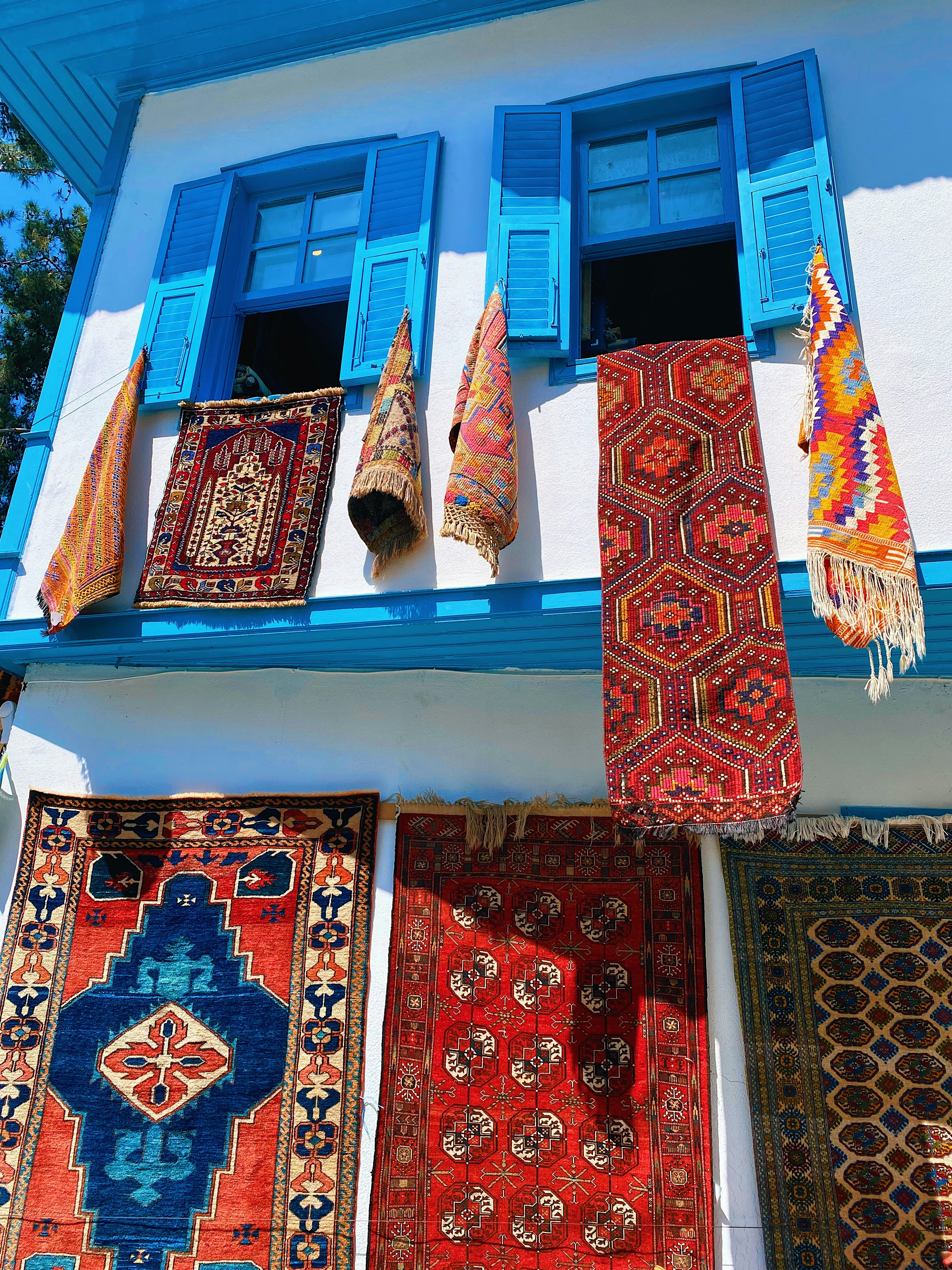 a bunch of rugs hanging outside of a blue window