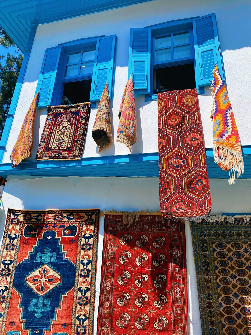 a bunch of rugs hanging outside of a blue window