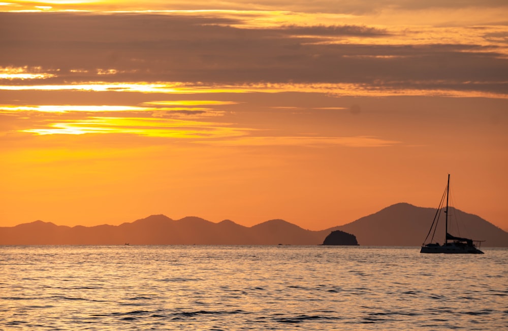 a sailboat floating in the ocean at sunset