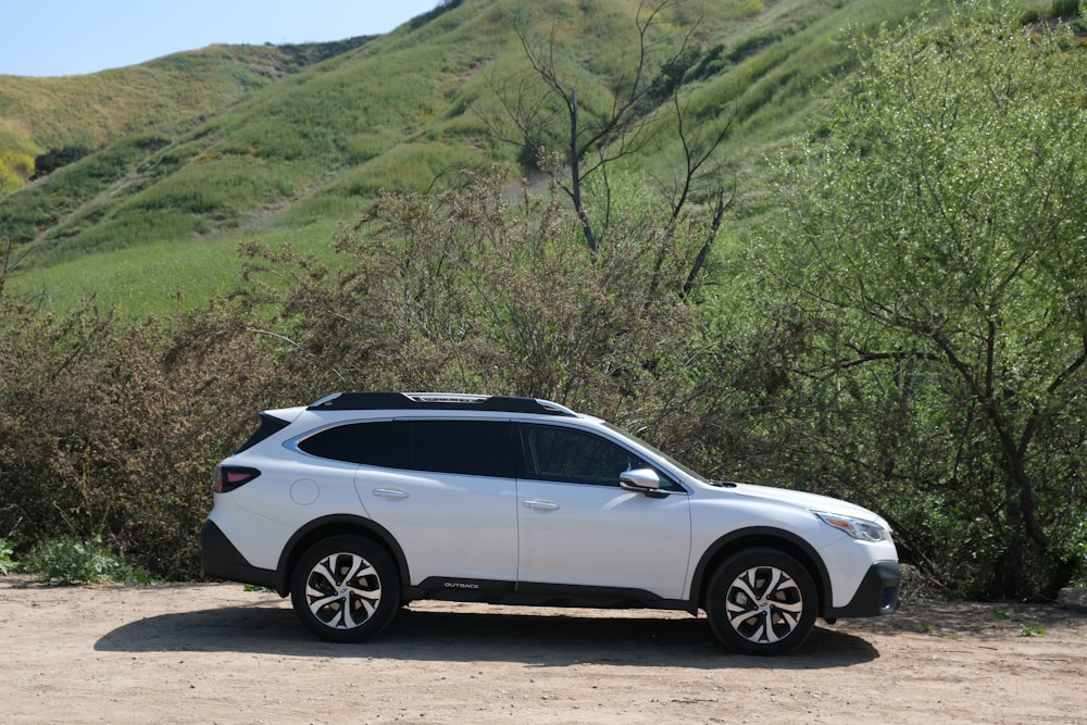 a white car parked in front of a lush green hillside