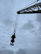 A large crane arm extends diagonally across the image with a heavy-duty hook hanging from it, silhouetted against a cloudy, overcast sky. The industrial equipment appears robust and weathered, highlighting its use in construction or lifting tasks.