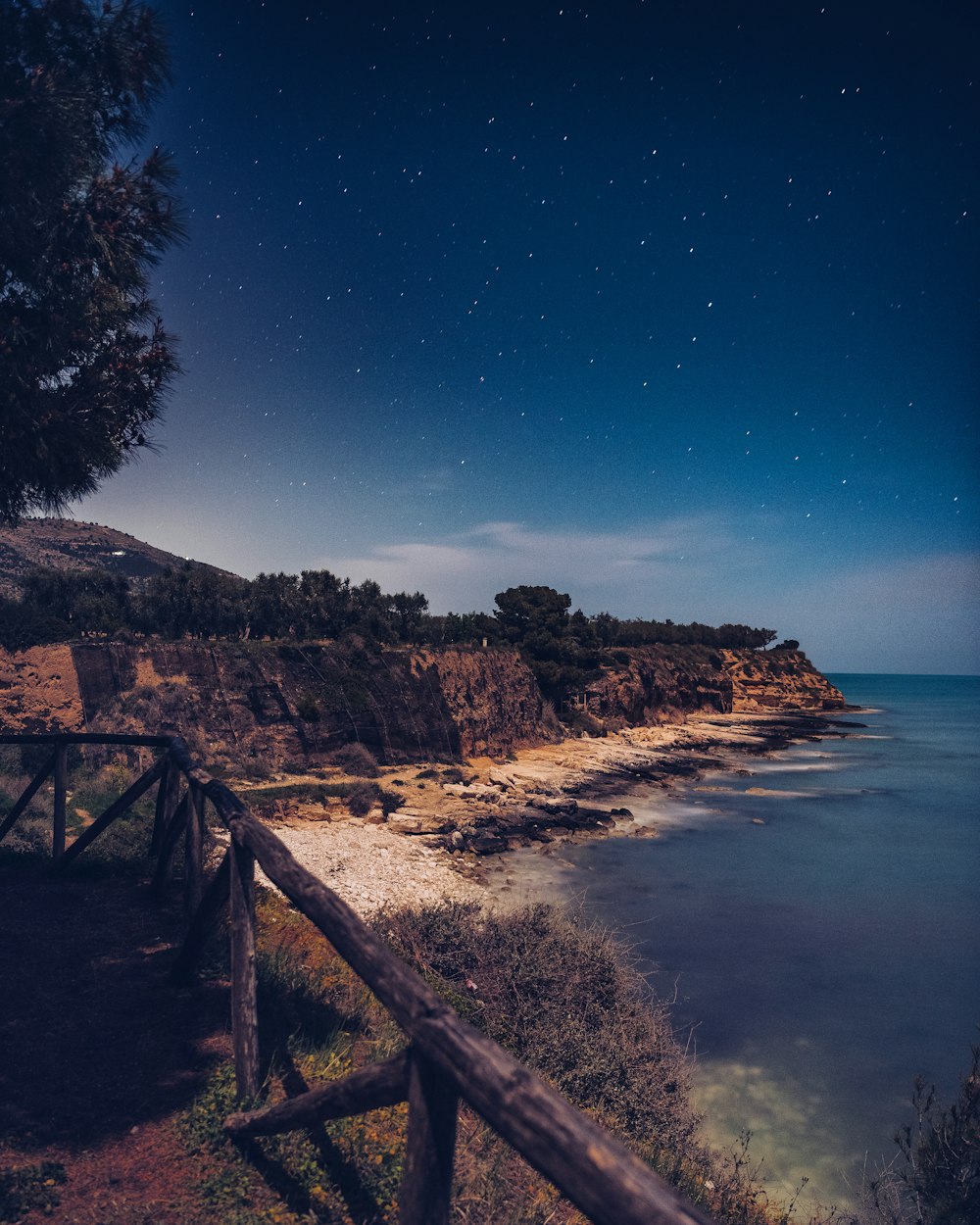 a night time view of a beach with a wooden fence