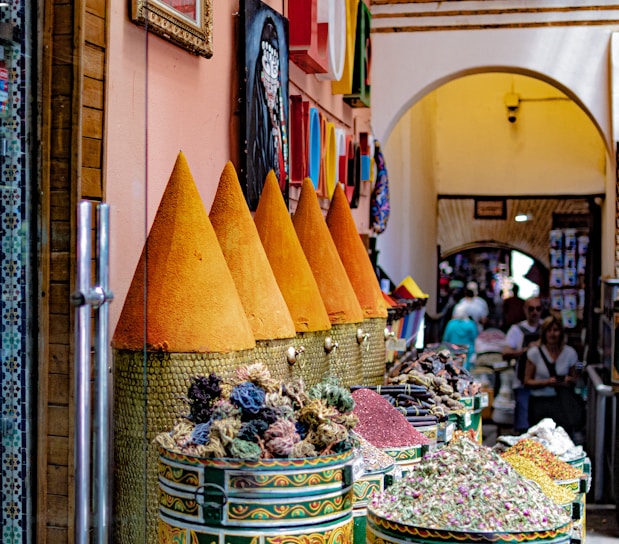 A vibrant market scene in Marrakech with colorful spices and textiles under bright sunlight.
