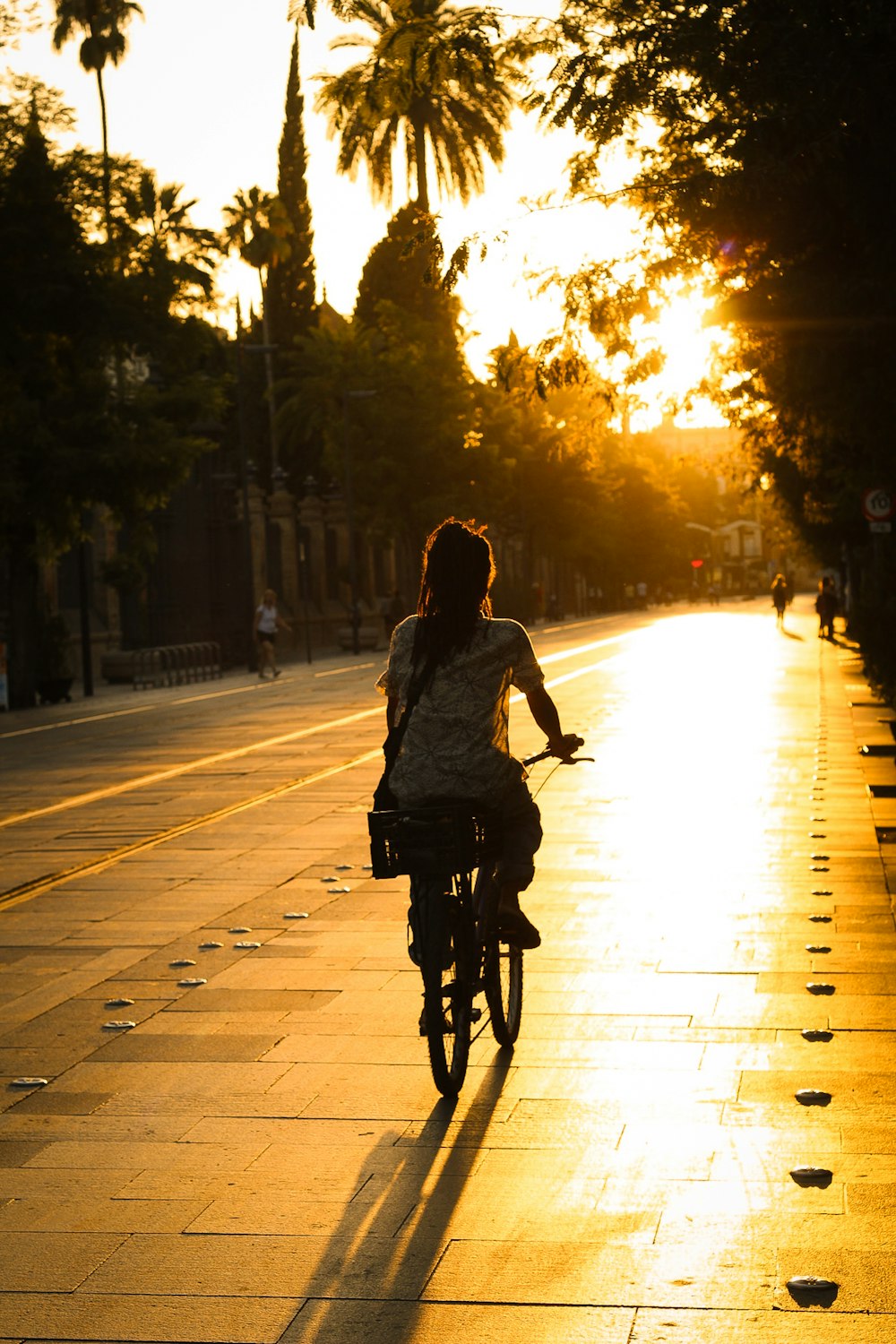 a woman riding a bike down a street at sunset