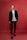 A person stands confidently against a solid red background, dressed in a stylish black suit with a white turtleneck. The outfit is completed with black loafers, and the individual has neatly groomed hair.