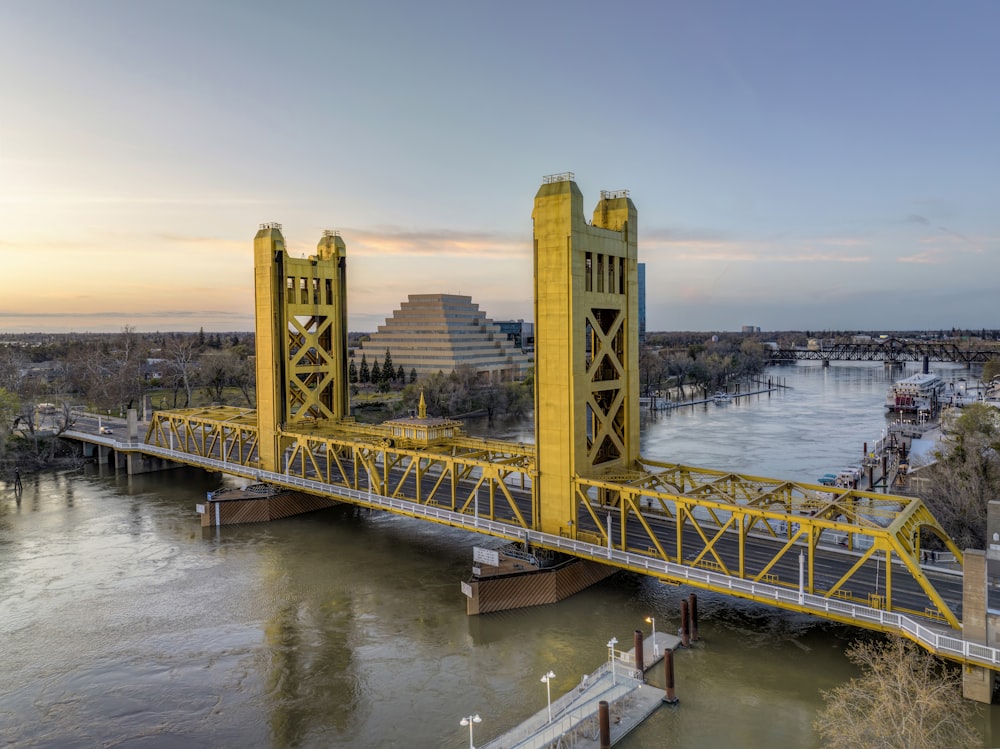 a yellow bridge over a river with a city in the background