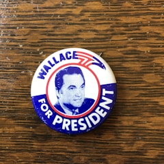 A close-up of a campaign button with 'Support Bob' text and Monroe County backdrop.