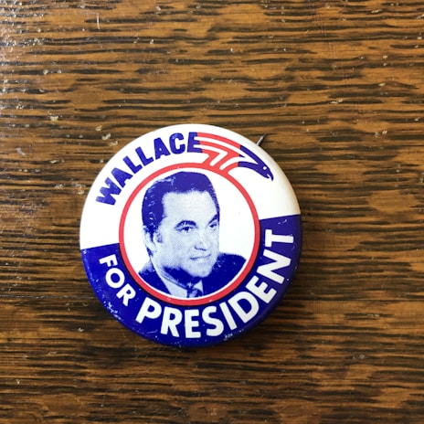 A vintage campaign button featuring a portrait with the text 'WALLACE FOR PRESIDENT.' The background includes red, white, and blue colors with a stylized eagle symbol.