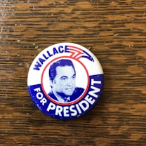 A vintage campaign button featuring a portrait with the text 'WALLACE FOR PRESIDENT.' The background includes red, white, and blue colors with a stylized eagle symbol.