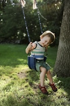 a little boy sitting on a swing in the grass