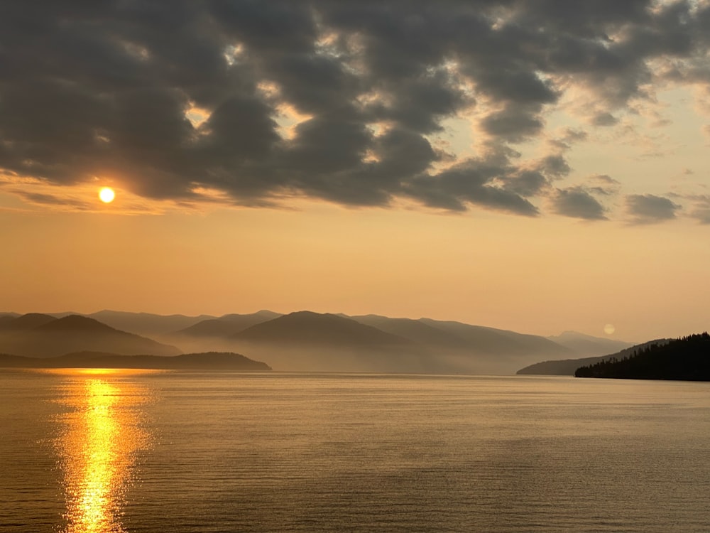 the sun is setting over a lake with mountains in the background