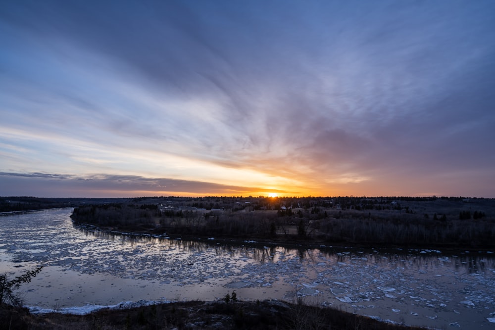 the sun is setting over a frozen river