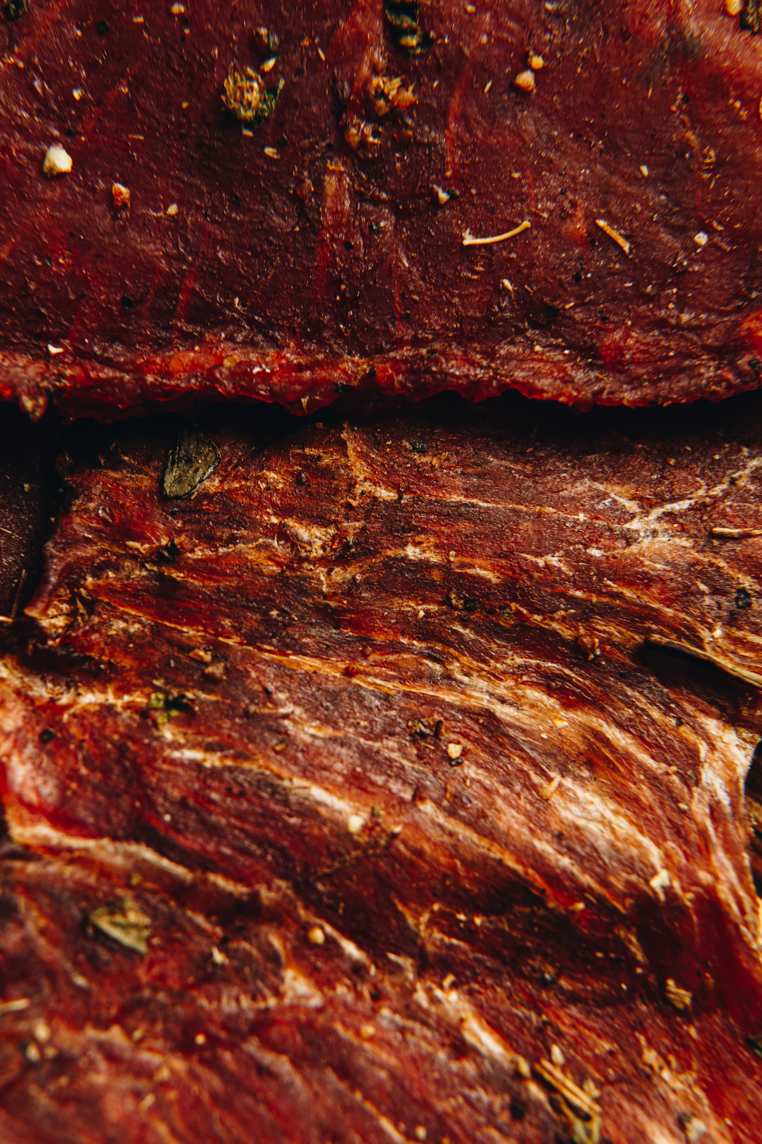 Close view of black-pepper beef jerky, the cracked pepper pressed into the glossy grain