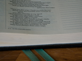An open book displaying text with a focus on certain passages that discuss spiritual and moral themes. The page is light-colored with black printed text and a teal ribbon bookmark partially visible at the bottom. The book rests on a wooden surface.