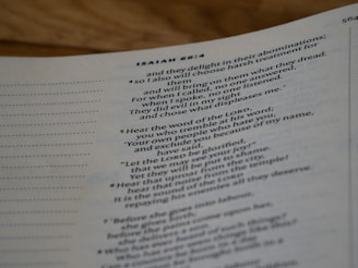 A close-up view of a page from a Bible, specifically from the book of Isaiah. The text is printed in black against a light-colored background, with verse numbers in a slightly bolder typeface. The page is viewed from an angle, and the text includes religious themes.