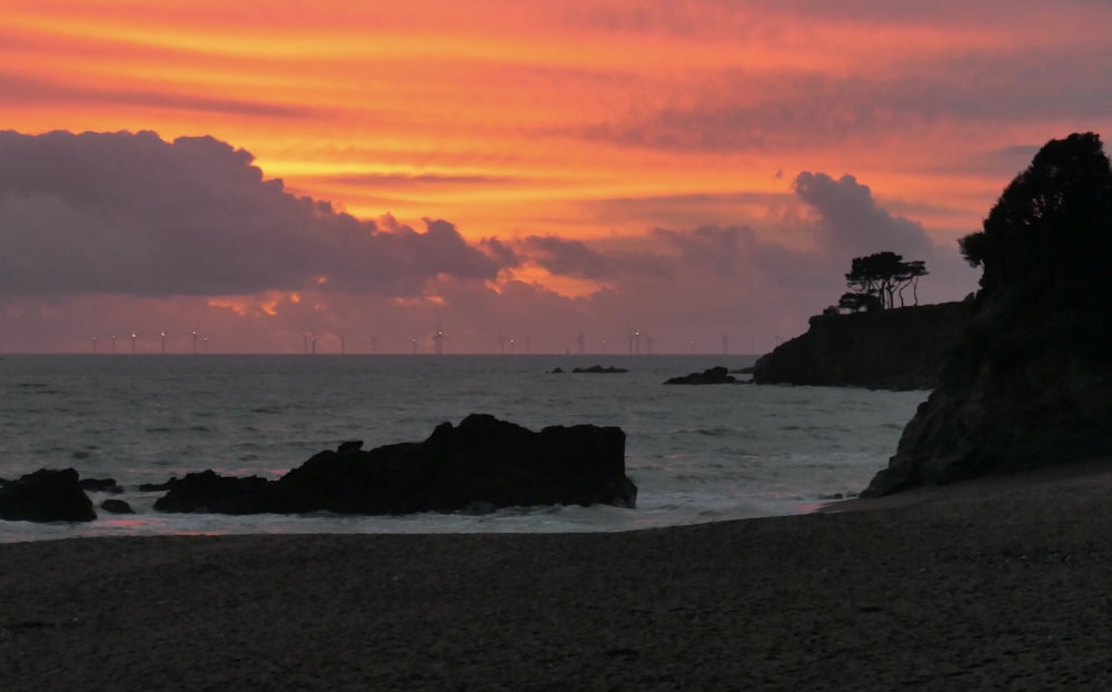 the sun is setting over the ocean with rocks in the foreground