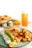 A breakfast plate featuring an omelette topped with avocado slices, salsa, and sour cream, served alongside crispy golden diced potatoes with garnish. A refreshing iced drink with lemon is placed at the side. The background includes some bread rolls and small bowls, likely containing condiments.