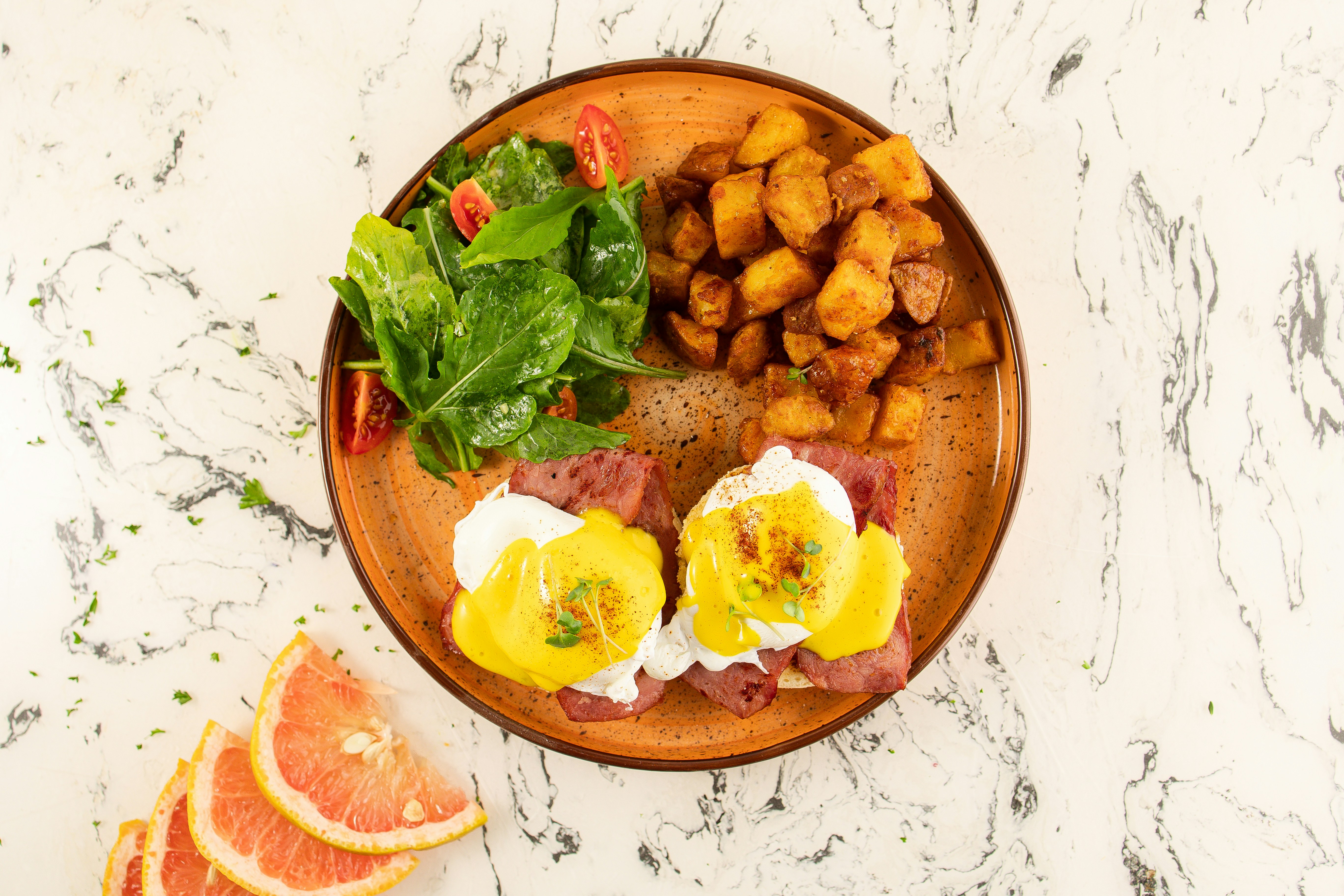 Overhead eggs benedict with potatoes and salad on marble