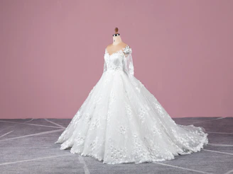 A softly lit photo of a delicate blush pink dress draped elegantly on a minimalist mannequin against a cream backdrop.