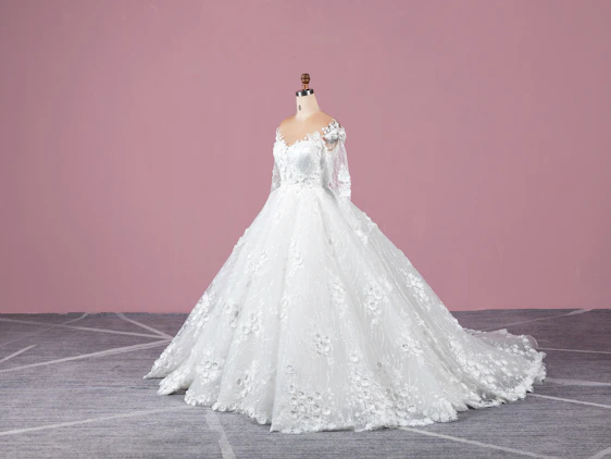 A softly lit photo of a delicate blush pink dress draped elegantly on a minimalist mannequin against a cream backdrop.