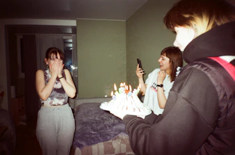 Friends laughing and using fun props inside a photo booth at a surprise birthday party.