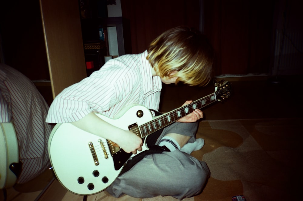 a young boy sitting on the floor playing a guitar