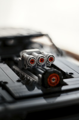 A close-up of a LEGO model showcasing a detailed assembly. The focus is on a set of three cylindrical pieces, each with red circular accents resembling thrusters or exhausts, mounted on a dark surface with rods and other mechanical components.