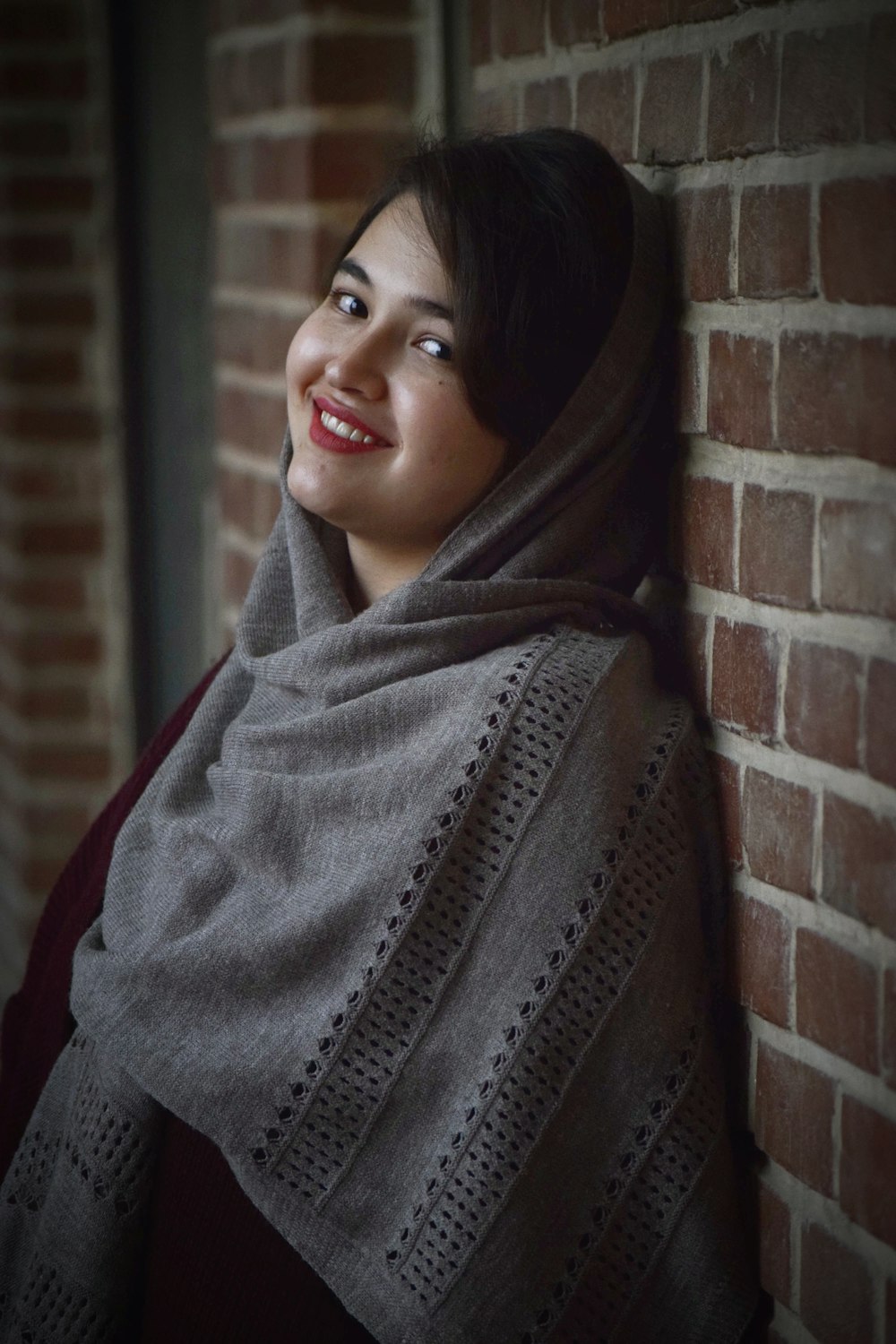 a woman wearing a shawl standing next to a brick wall