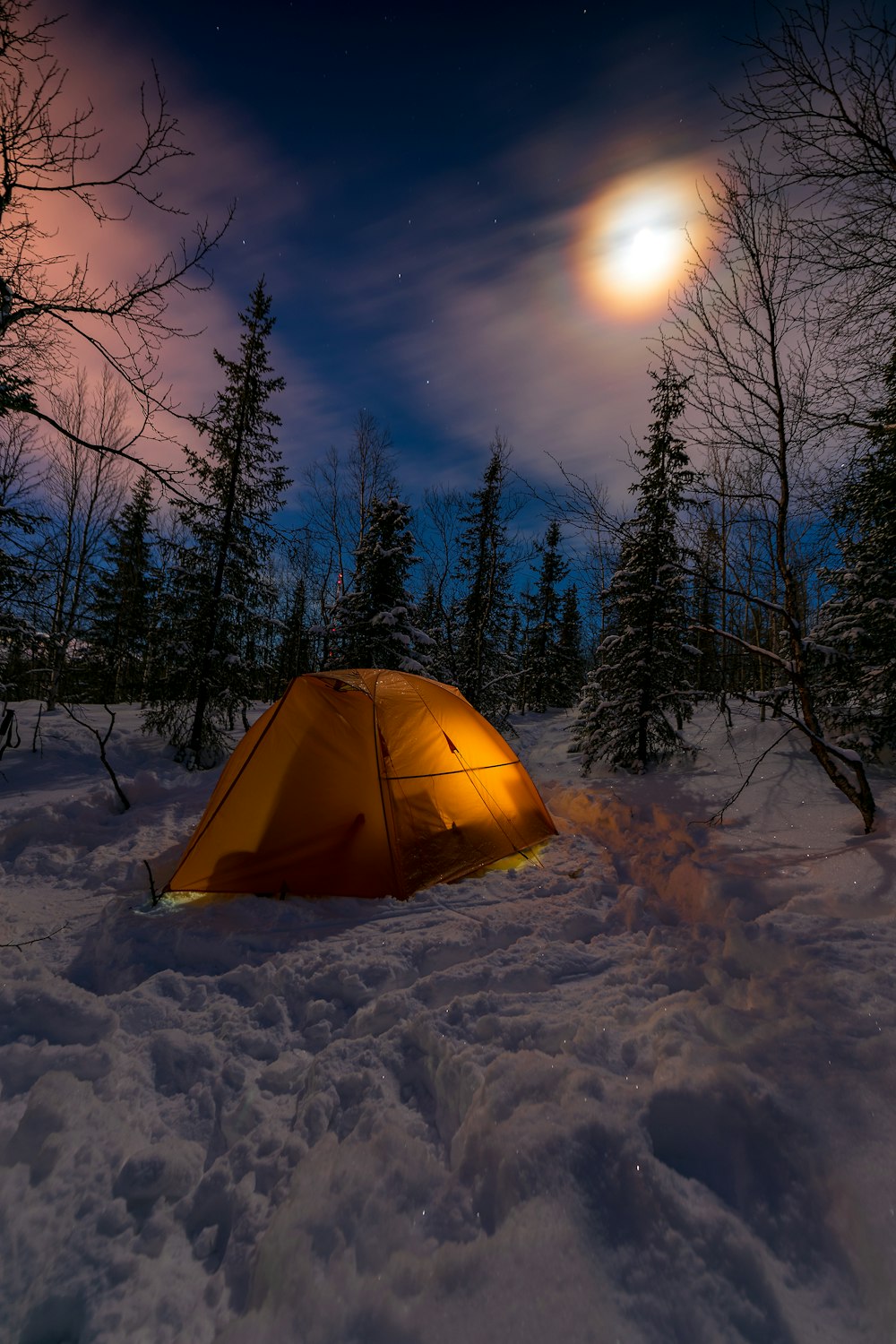 a tent pitched up in the snow with a full moon in the background