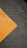 A textured asphalt surface with a prominent diagonal yellow paint stripe running across it. The paint appears slightly worn, contrasting against the dark, rough texture of the asphalt.