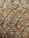 Intricate silver embroidery designs create a repeating pattern on a rich, textured brown fabric. The motifs include floral elements and ornate scrolls, giving it an elegant and luxurious appearance.