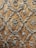 Intricate silver embroidery designs create a repeating pattern on a rich, textured brown fabric. The motifs include floral elements and ornate scrolls, giving it an elegant and luxurious appearance.