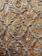 Intricate silver embroidery designs create a repeating pattern on a rich, textured brown fabric. The motifs include floral elements and ornate scrolls, giving it an elegant and luxurious appearance.