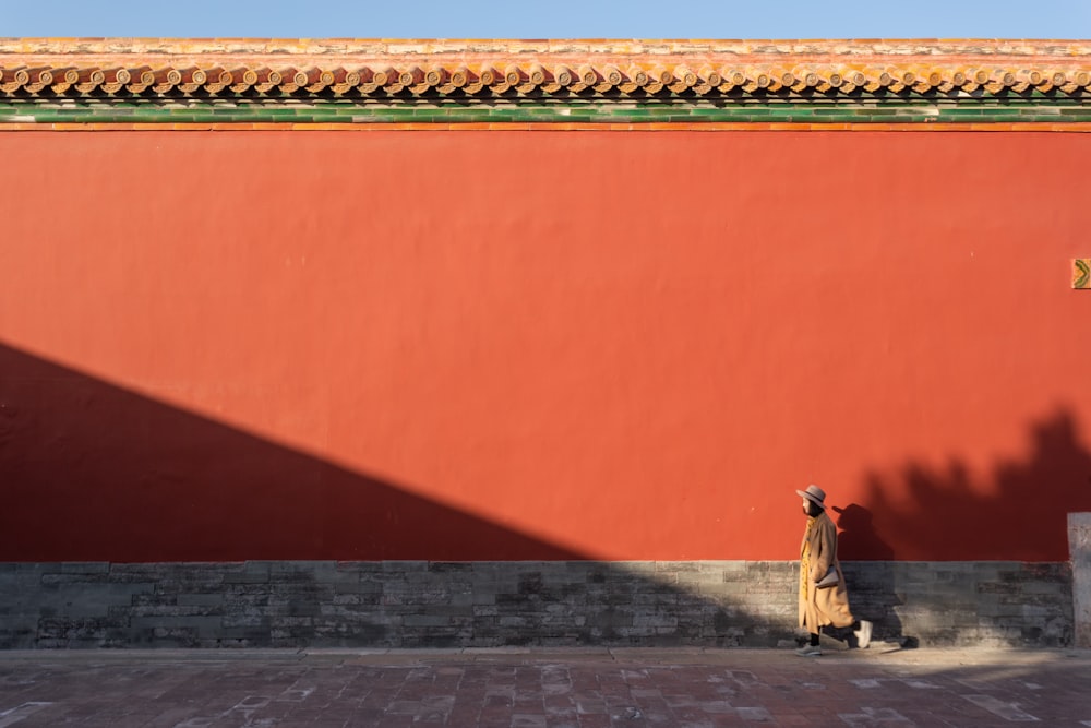 a woman walking down a street past a red wall