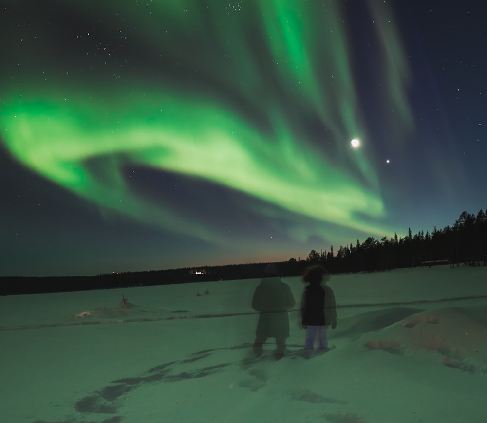two people standing in the snow watching the aurora bore