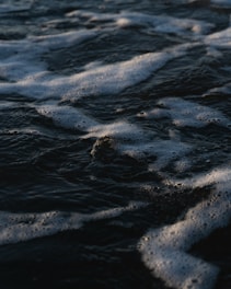 Dark ocean water with waves creating patterns of foam on the surface.