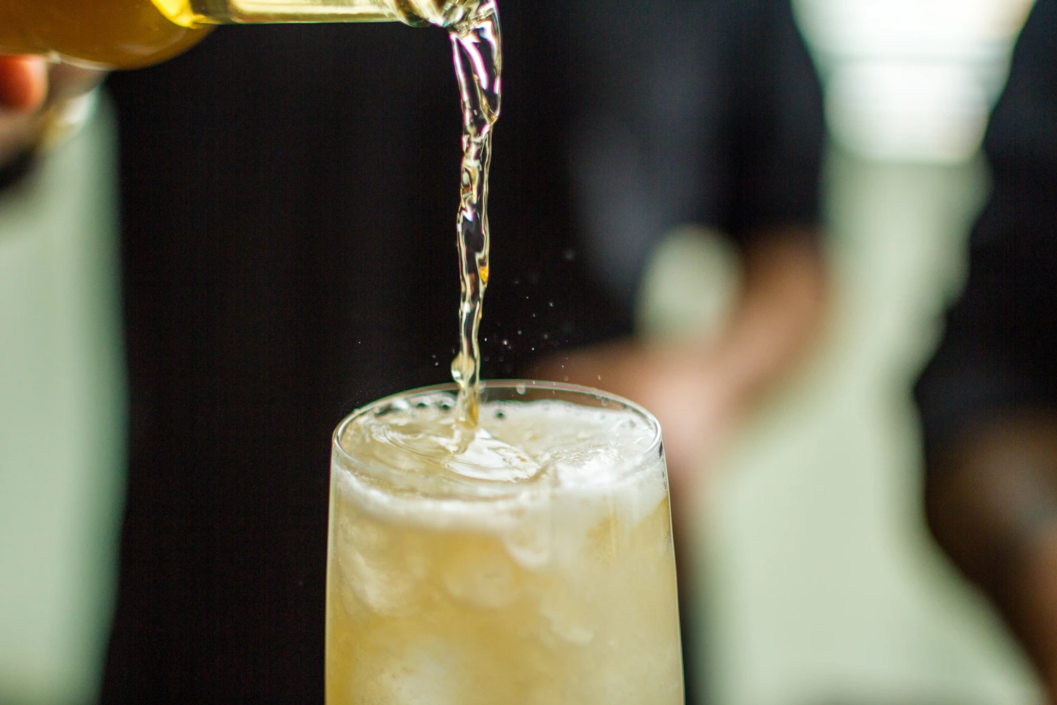 Ginger ale poured from a bottle into an iced glass, a stream of bubbles in mid-air