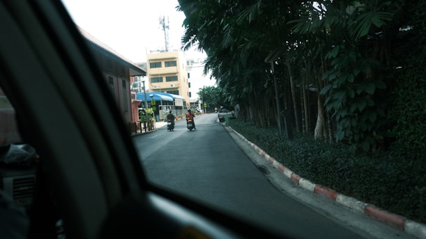 a man riding a motorcycle down a street next to a lush green forest