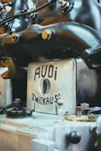 A close-up view of an antique or vintage engine with a metallic finish, featuring branding that reads 'AUDI ZWICKAU.' The machine components, including bolts and pipes, suggest an industrial or mechanical setting.