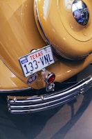 A vintage yellow car displays a Texas license plate with the number 133 VNL. The rear features chrome details, including a bumper and a round emblem. A classic design is highlighted by a polished metal surface, red lighting, and decorative elements.