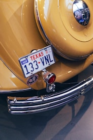 A vintage yellow car displays a Texas license plate with the number 133 VNL. The rear features chrome details, including a bumper and a round emblem. A classic design is highlighted by a polished metal surface, red lighting, and decorative elements.