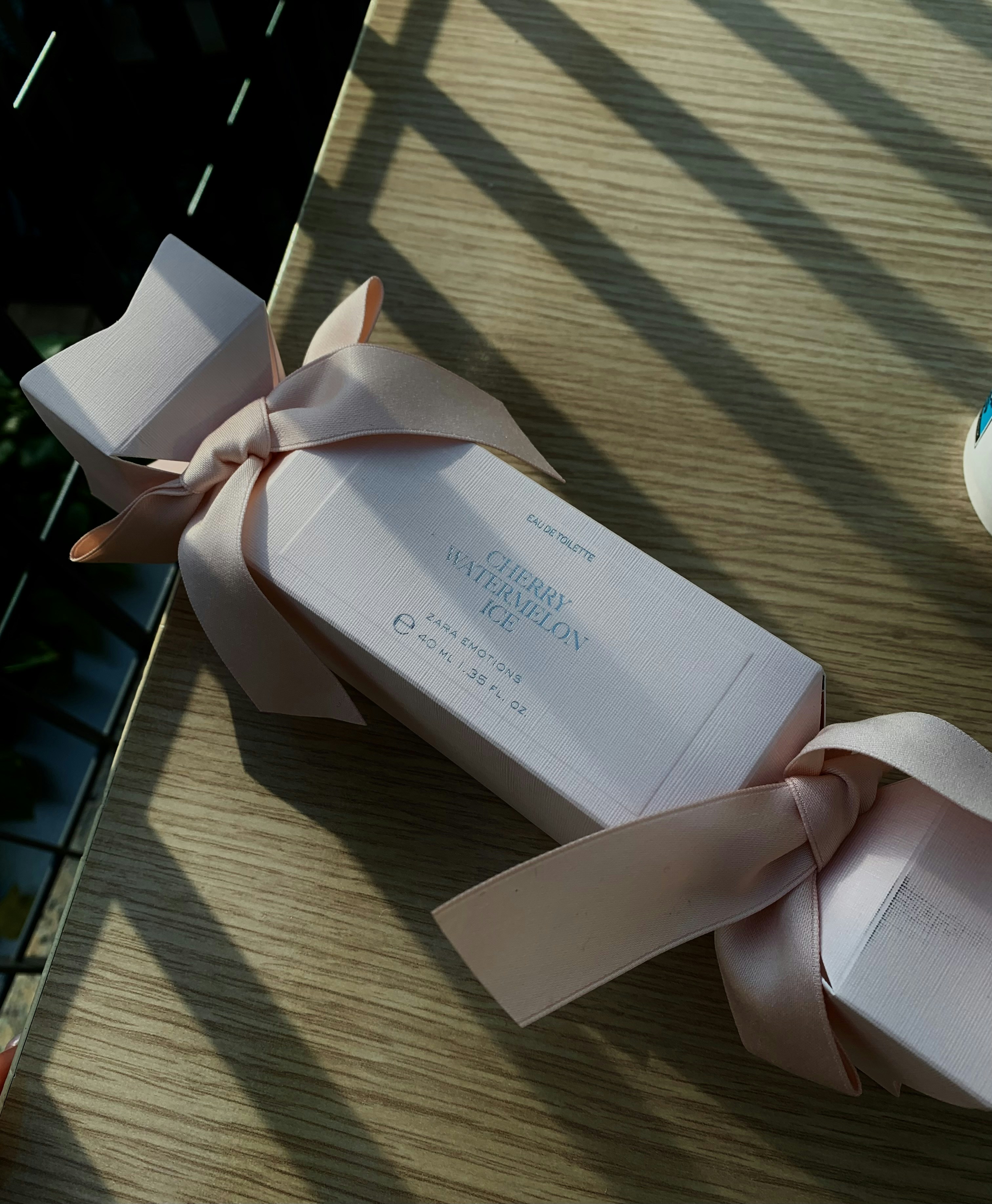 Pink gift box with satin ribbon surrounded by beauty products on soft cream background